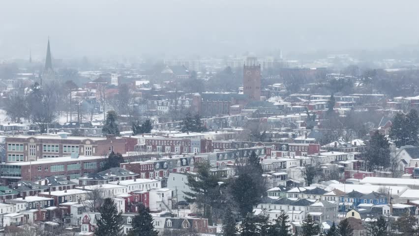 Aerial view of York, Pennsylvania covered in snow with fog and mist softening skyline, with historic buildings, residential neighborhoods and church towers in calm winter atmosphere. Christmas time.