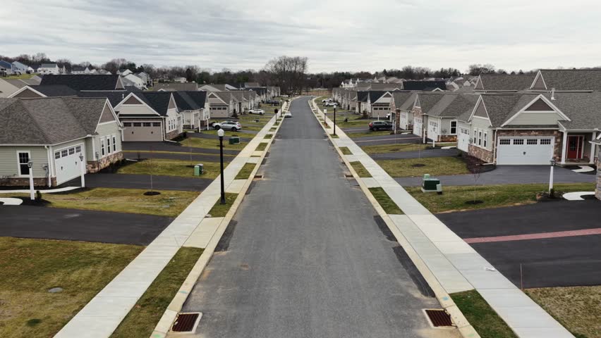 Aerial forward view of modern suburban neighborhood in USA with newly built single-family homes with garages, driveways and uniform streets in quiet residential development. Pennsylvania, USA.
