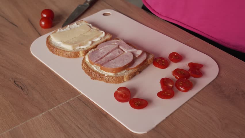A woman stuffs a sandwich with sausage and tomatoes. Cooking at home.