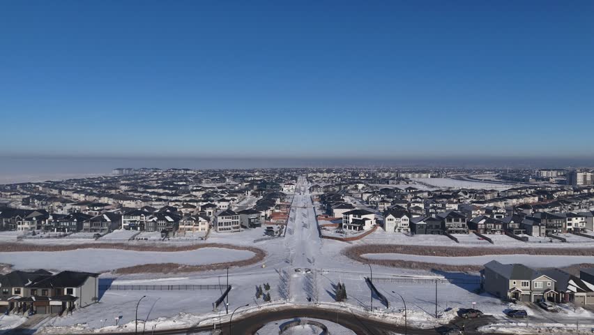 High aerial drone shot following a path in Bridgwater Winnipeg Manitoba. Snow covered ground with clear sky as drone tracks along pathway in winter.