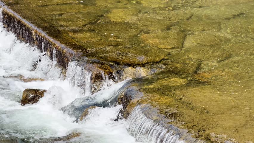 Static high angle shot of clear river water flowing over mossy stone steps in Kyoto