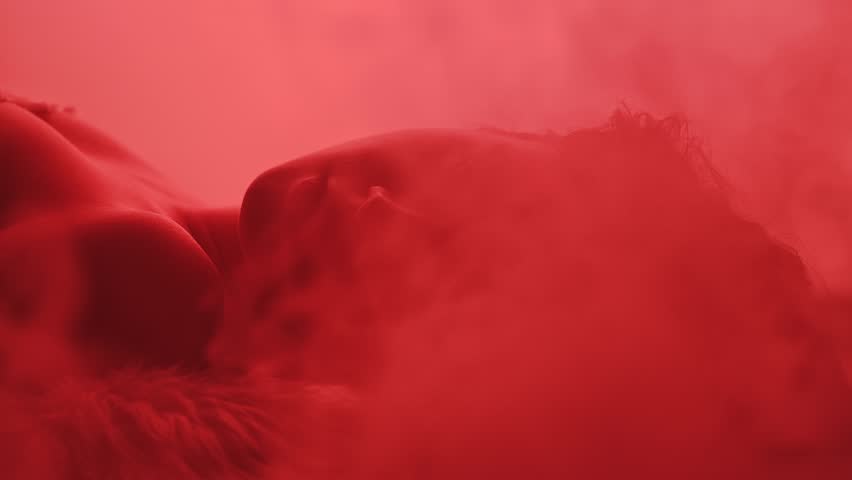 The silhouette of a young woman lying in smoke is illuminated by changing multicolored lights. Color beauty.