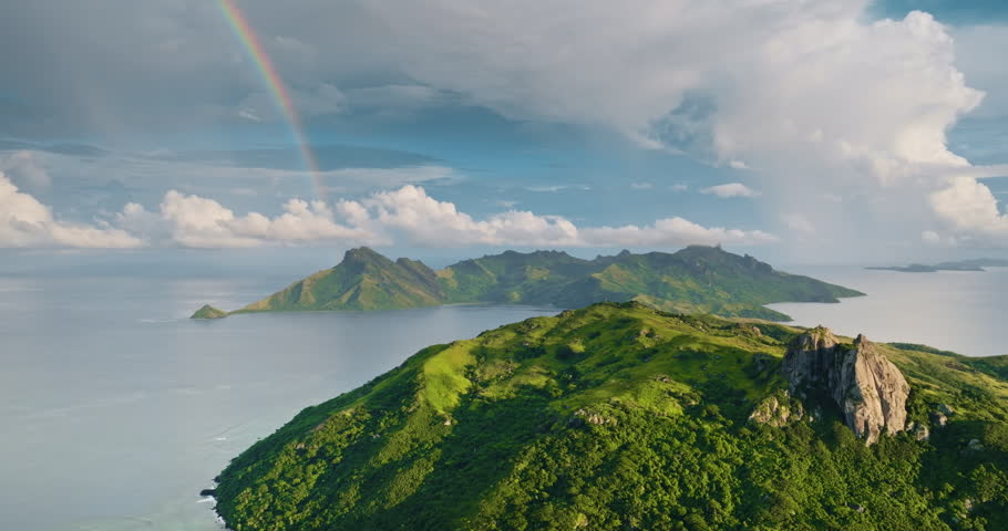 Yasawa Islands, Fiji: striking colorful rainbow arching over lush green volcanic mountains and pristine Pacific Ocean, revealing a tropical paradise nature landscape. Aerial view drone flight panorama