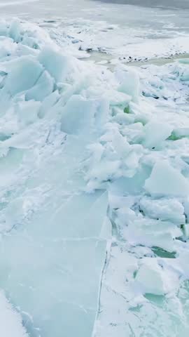 Close-up of a pressure ridge with shattered sea ice and pale turquoise slabs on a frozen shoreline, rugged winter texture and natural abstract pattern in a vertical frame.