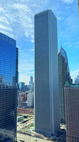 Tall reflective buildings are seen in a city with a clear sky and clouds above during the daytime.
