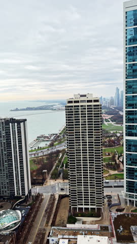 Tall buildings and lakefront can be seen from a high point in Chicago with a cloudy sky and open water in the distance.