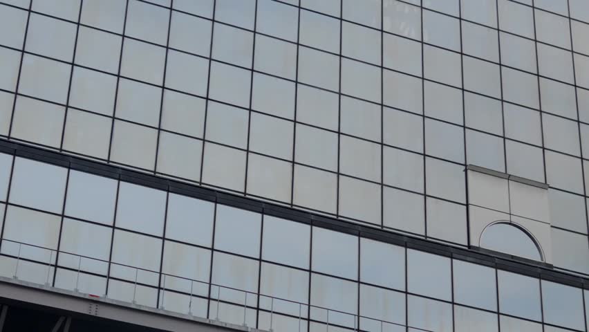 A panning shot showcasing the iconic Kyoto Tower reflected in the windows of a modern building, captured from the bus platforms of Kyoto Train Station in Kyoto, Japan.