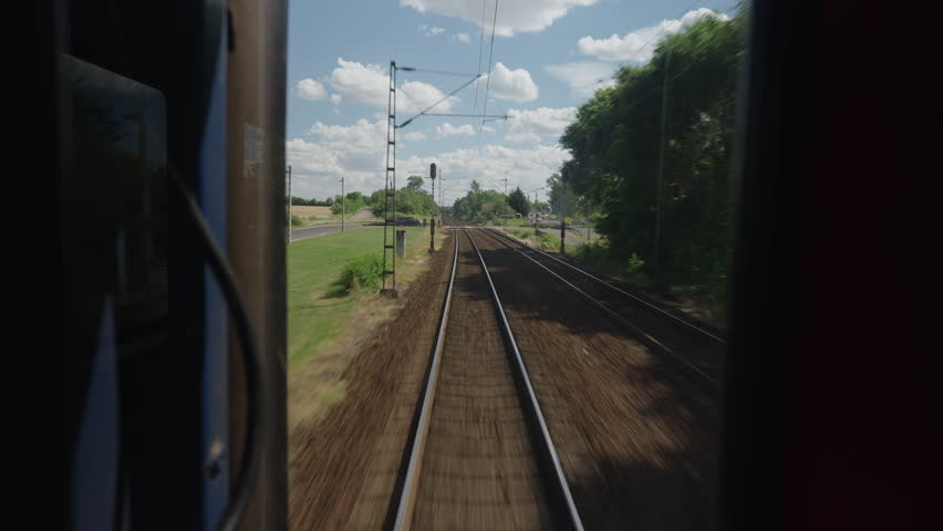 Point of view from the back of a moving train. Railway tracks receding into the distance as the train travels through the countryside