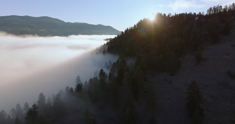 Sunlight breaking over mountain ridge above fog covered forest valley Montana, backlit silhouette casts shadow