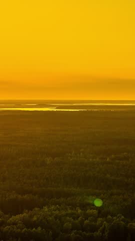 An orange glowing sky over the woods and a lake in the distance during sunset.