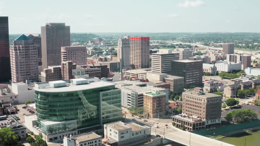 Close-up aerial drone view of Dayton, Ohio skyline, smooth cinematic motion moving right to left, modern buildings and urban architecture in sharp detail, natural daylight, clear sky, realistic cityscape footage.