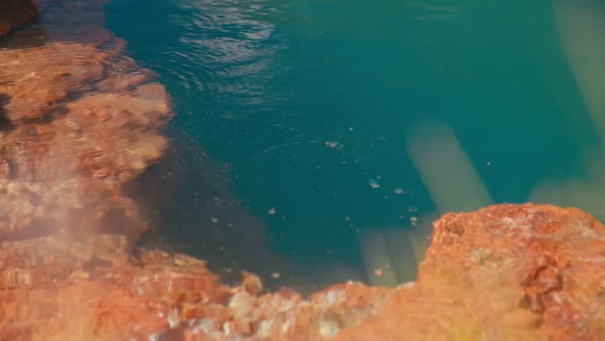 Close up of a bubbling mineral spring with deep blue water and red rock formations, highlighting vivid colors, natural carbonation, and striking geological patterns.