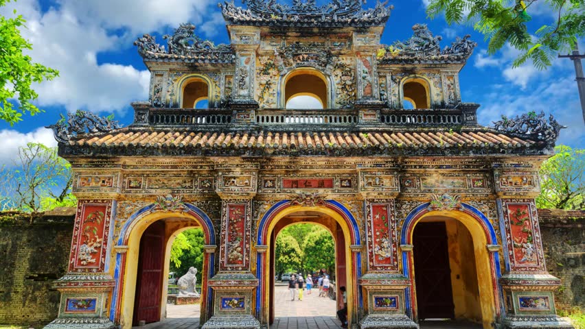 The ancient gate-bastion of the Imperial Forbidden City on a cloudy day. Hue, VietnamHien Nhon Gate and eastern entrance of the UNESCO World Heritage site of Imperial Palace and Citadel in Hue, VietnamHue, Vietnam  Ornate, weathered gate of Hien Nhon in the Imperial City of Hue, Vietnam, with intricate carvings, multiple archways, and surrounding greenery under a bright sky.