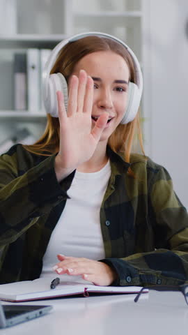 Woman influencer recording video blog on smartphone sitting at an home office desk. Girl sits front mobile phone camera on tripod records educational tutorial video recounts personal lifestyle blog