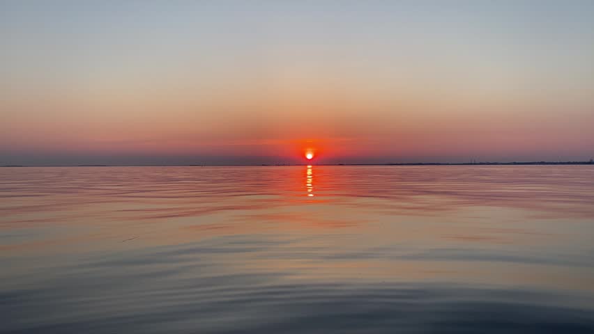 Golden sun setting over a calm sea horizon with vibrant orange and purple sky reflecting on the smooth water surface.