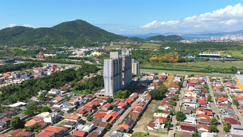 Drone view of residential towers along Rodovia Beto Carrero World (SC-414) in Armação, Penha, Santa Catarina, Brazil, with Praia da Armação do Itapocorói and Serra do Mar hills in background.