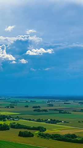 Drone view of white clouds forming in a blue sky over a rural landscape with meadows and trees.
