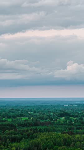Drone view of dark gray clouds drifting quickly across the sky over a wooded landscape.