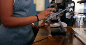 Unrecognizable african american female barista wearing an apron entering an order on a point of sale touchscreen tablet, managing transactions and serving customers in a modern coffee shop - Powered by Shutterstock - Get 15% off with code: PIKWIZARD15