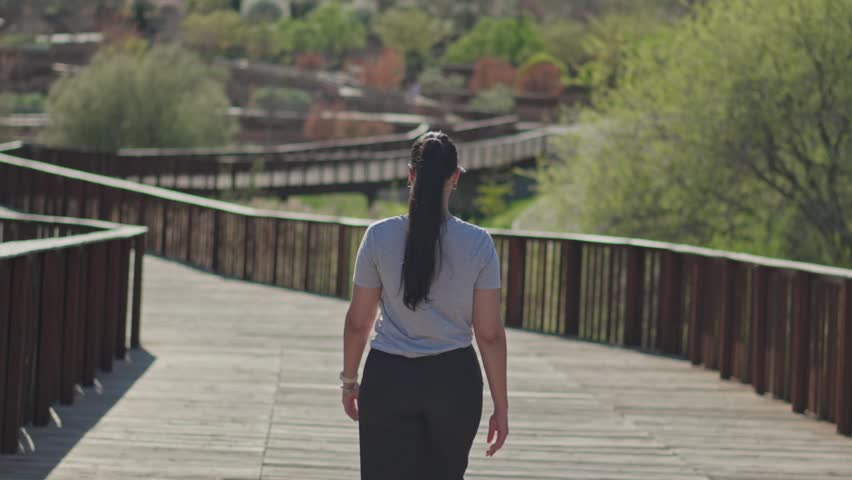 Back view of a young woman crossing a bridge in a green nature park