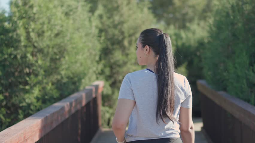 Back view of a young woman crossing a bridge in a green nature park