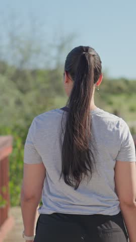 Back view of a young woman crossing a bridge in a green nature park