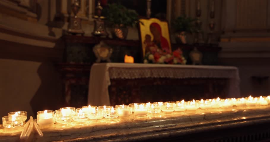 Votive candles on a marble altar in a dim church, static shallow focus keeps front flames crisp while the background melts into bokeh showing a blurred icon of the Madonna with Child and soft golden reflections on stone
