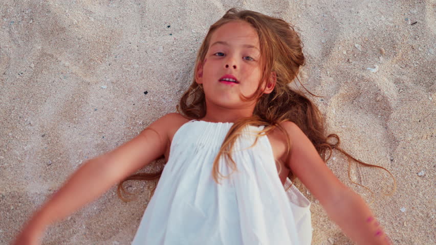 A little beautiful girl in a white sundress has fun on the beach of a tropical island on vacation at sunset