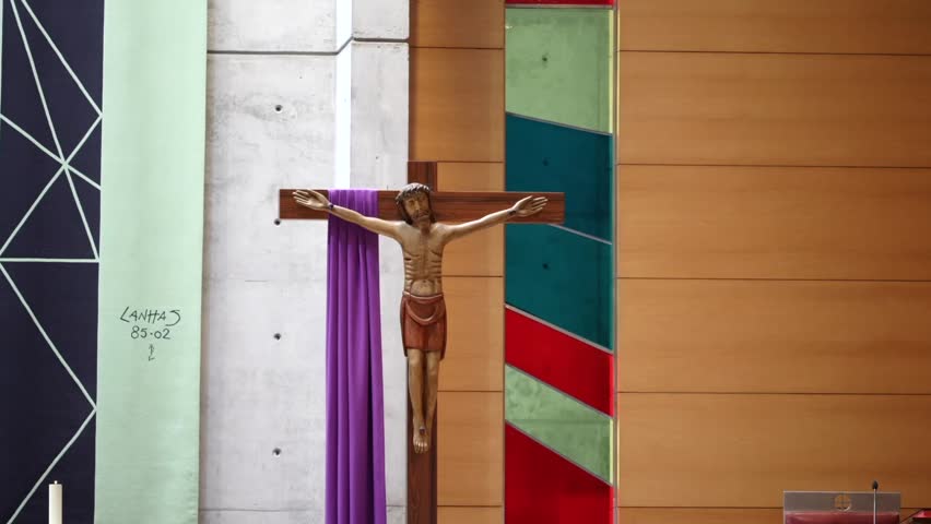 Jesus Christ statue on wooden cross inside church with purple cloth and geometric wall panels in religious worship space