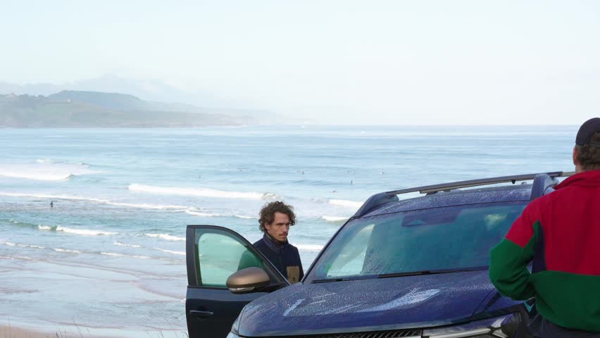 Two young people getting out of an SUV in the middle of a green meadow with mountains in the background
