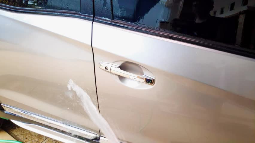 Man hand holding a hose pipe to wash a silver vehicle with slow motion water spray