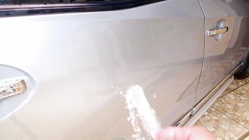 Man hand holding a hose pipe to wash a silver vehicle with slow motion water spray