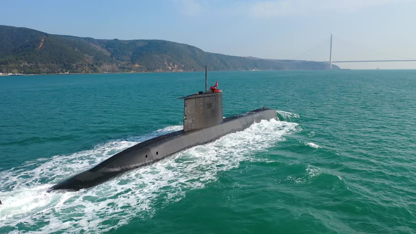 Turkish navy submarine underway at full speed in Bosphorus with stern and rudder plane visible, sea foam wake and Yavuz Sultan Selim Bridge in background