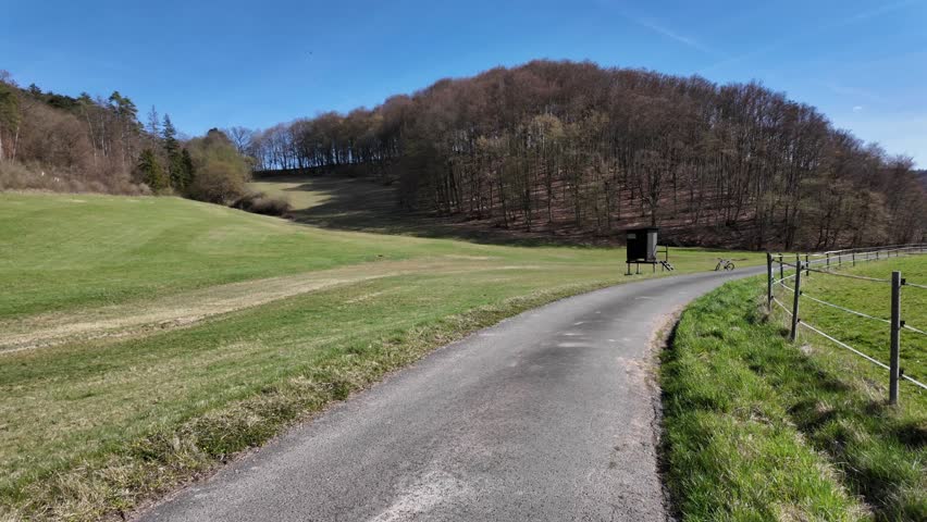 Narrow country road passing through green fields. Scenic rural landscape with hills and blue sky. 