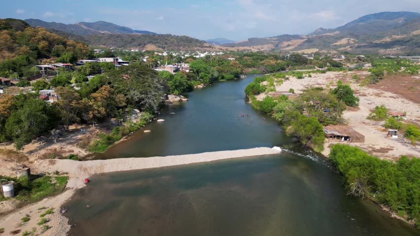Stunning aerial panorama of the Tecpan de Galeana River in Guerrero, Mexico, showcasing lush nature, surrounding mountains, and a vibrant local village life from a drone perspective.