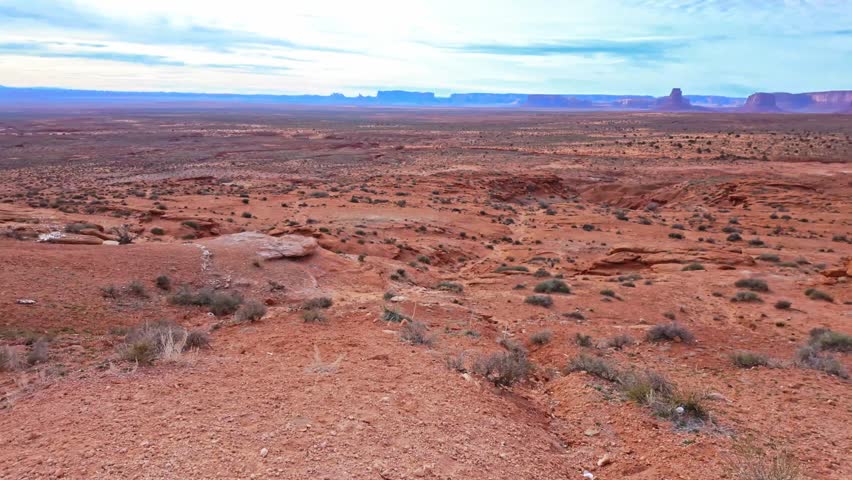 Wide panoramic landscape shows Brigham Tomb with West and East Mitten Buttes across Monument Valley desert terrain in Arizona