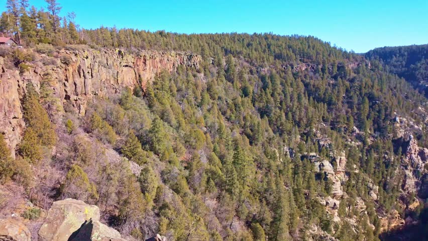 Expansive aerial landscape of Oak Creek Canyon shows forested cliffs and winding terrain under bright sunlight in Arizona