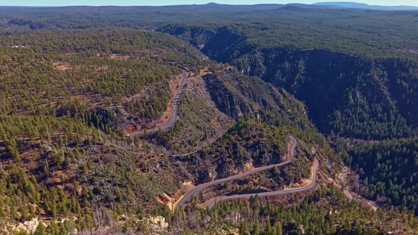 Expansive aerial landscape of Oak Creek Canyon shows forested cliffs and winding terrain under bright sunlight in Arizona