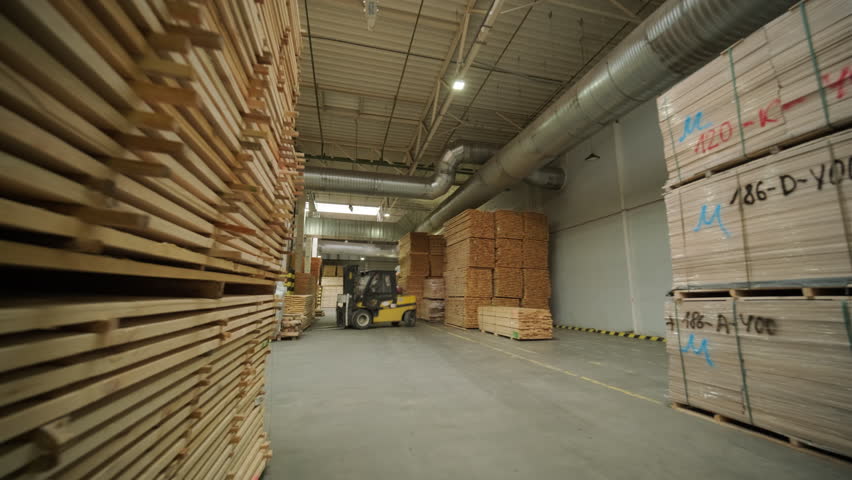 A large industrial warehouse featuring a forklift operating among stacks of dried wooden planks prepared for further furniture or flooring production
