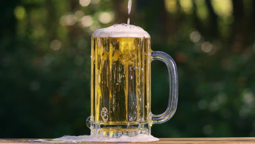 Beer pours slowly with foam. Beer pour in glass with bubbles and foam. Beer on outdoor summer background. Beer pour in closeup.