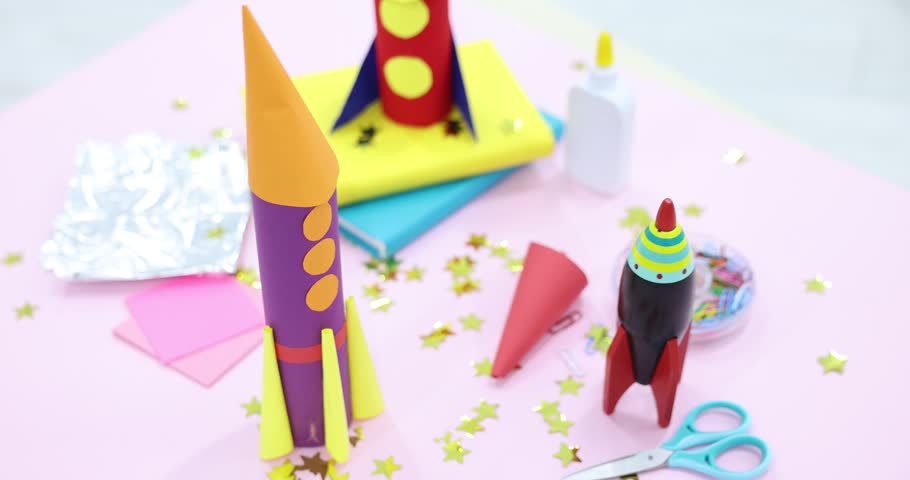 Toy and handmade rockets on light pink background, closeup