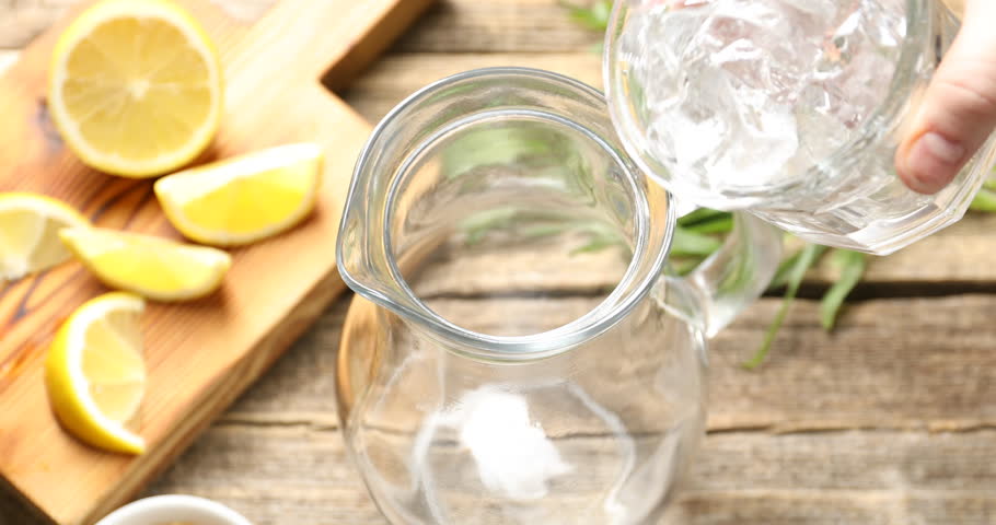 Woman making tasty lemonade with tarragon, ice cubes and lemon at wooden table, closeup