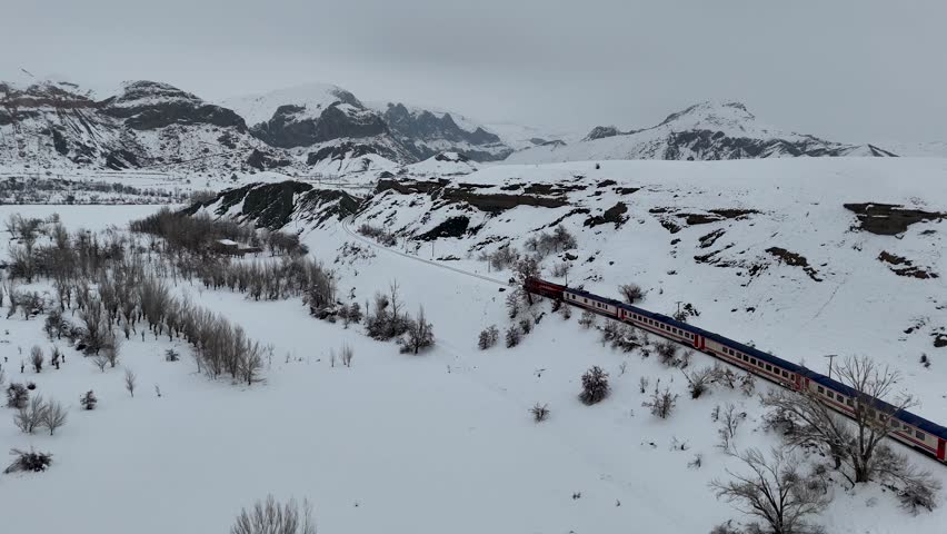 Touristic Eastern Express passenger train traveling through a snowy valley and along a river in Eastern Anatolia, Turkey.