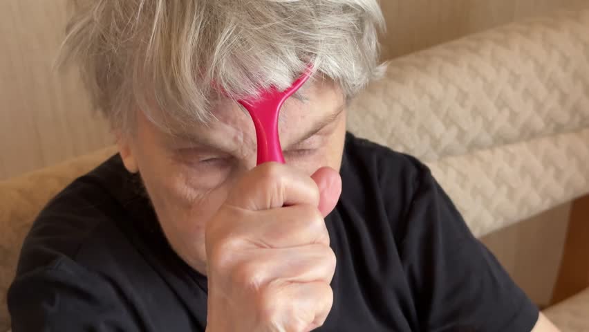 Elderly Caucasian woman massaging scalp gently close-up sequence of senior selfcare using red plastic finger massager along temple.