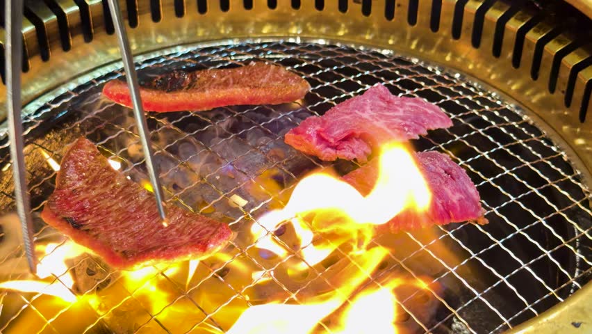 Close-up shot of raw marbled beef cooking on a charcoal grill with flickering orange flames