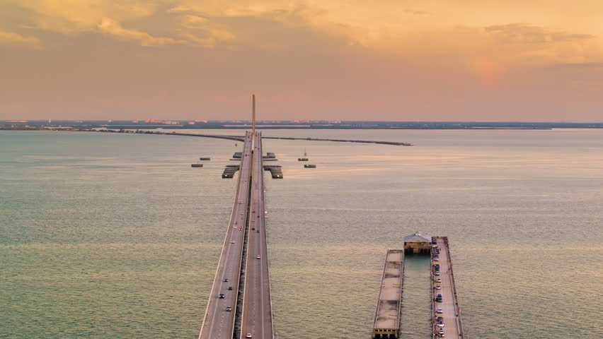 Fishing pier and highway road at sunset. Driving traffic cars on Sunshine Skyway Bridge over Tampa Bay in Florida. Transportation infrastructure in USA