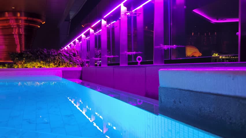 A modern swimming pool with bright neon lighting, reflections in the water and stylish architecture of the night space.
