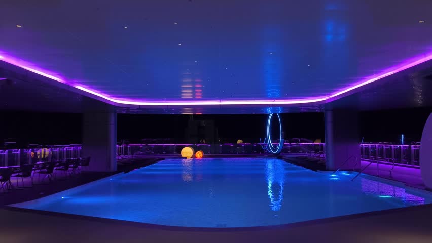 A modern swimming pool with bright neon lights and reflections in the water creates an atmosphere of relaxation and luxury at night.