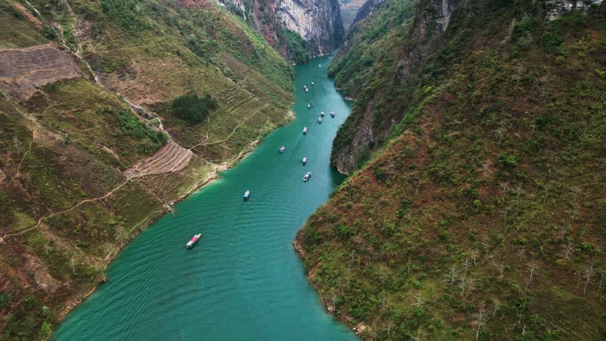 Aerial drone footage of Nho Que River flowing through Tu San Canyon with towering limestone cliffs turquoise water small boats and a deep mountain gorge in northern Vietnam