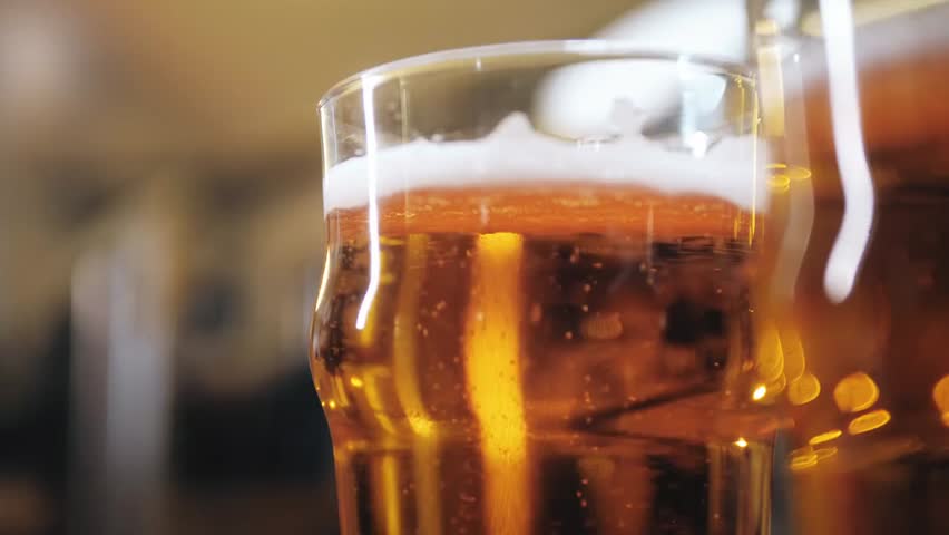 Closeup of foamy golden beer in glass mugs on a pub bar counter, fresh pale ale with rich foam texture, refreshing drink in a lively nightlife setting.